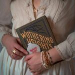 A woman in a vintage dress holding the classic book 'Wuthering Heights' with artistic jewelry.