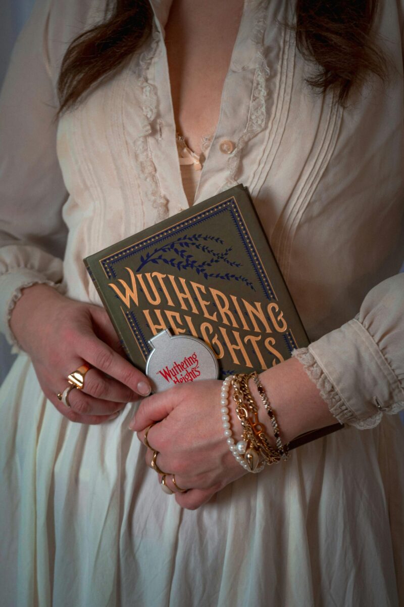 A woman in a vintage dress holding the classic book 'Wuthering Heights' with artistic jewelry.
